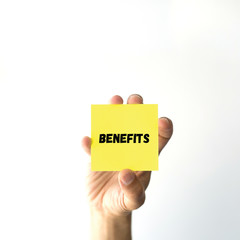 Hand holding yellow sticky note written BENEFITS word