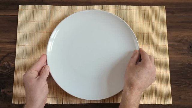 The man puts on wooden table from the old boards with napkin made of bamboo white round dish and metal fork