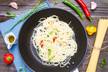Spaghetti Aglio Olio e Peperoncino on Roasting Pan. Top View Italian Dish with Raw Cooking Ingredients on Wooden Background.