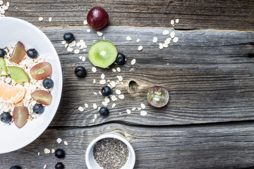Fototapeta na wymiar Oat Flakes with Fresh Fruits and Chia Seeds on Wooden Background with Empty Space for Design