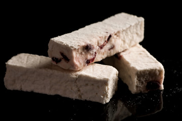 Three pieces of turkish delight with berries on a black reflective surface