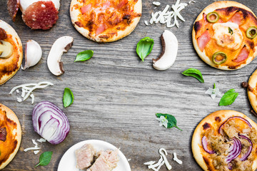 Top View of Different Types of Small Pizza with Ingredients and Empty Space in the Middle on Wooden Background