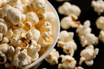 Popcorn in a white ceramic bowl on a black wooden table, selective focus