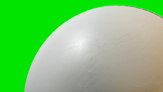 A closeup of a traditional white cricket ball with a leather stitched surface rotating once to create a loop able sequence on a green screen background - 3D render