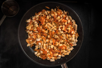 Fried chicken, onions and carrots in the pan on a dark background, top view