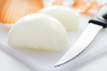 Yellow onion peeled and cut in half on a white chopping board