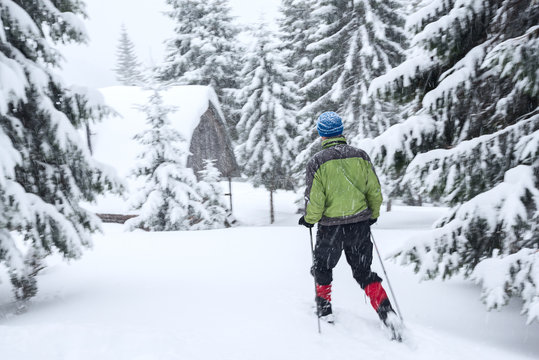 Traveler in snowshoes goes to the wooden hut