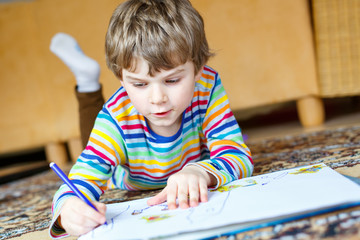 preschool kid boy at home making homework, painting a story with colorful pens