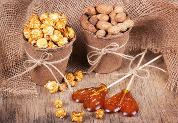 Fototapeta premium Paper bucket of caramel popcorn, roasted peanuts in shell, and lollipops. Set meal for a movie. Not healthy food and snacks