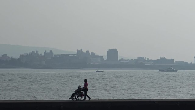 Personal healthcare walking together a paraplegic person in wheelchair on the waterfront of Tamshui, Taiwan-Dan
