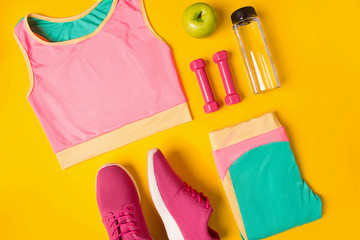 Fitness accessories on yellow background. Sneakers, bottle of water, dumbbells and sport top.