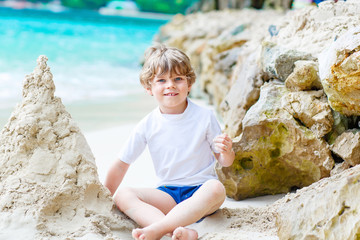 Fototapeta na wymiar Little kid boy building sand castle on tropical beach