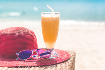 Orange fresh juice, hat and sunglasses near sea