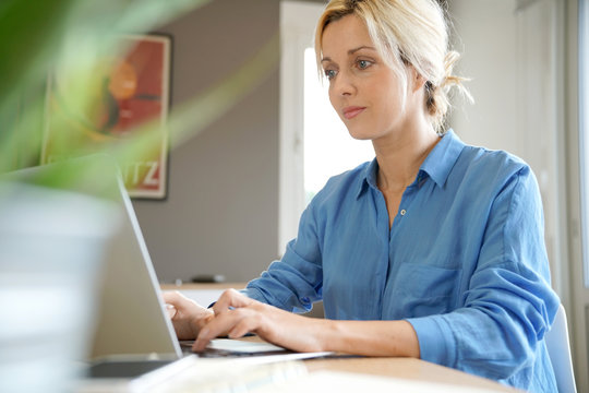 Portrait Of Blond Woman With Blue Shirt Working From Home On Laptop