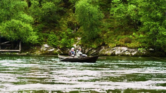 Lockdown shot of senior man rowing boat while friend fishing on river
