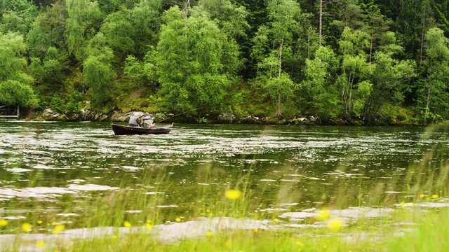 Dolly shot of senior men rowing boat while fishing on Nordic river by trees
