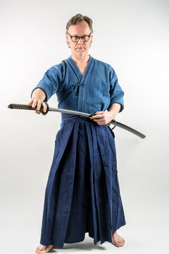 Adult caucasian male with glasses training Iaido drawing a Japanese sword with focused look. Studio shot with white background.