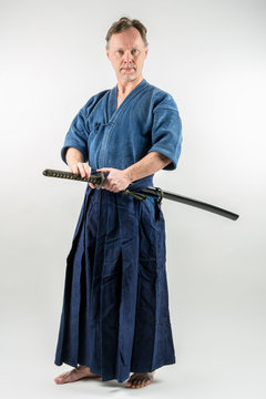 Adult caucasian male training Iaido about to draw a Japanese sword with focused look. Studio shot with white background.