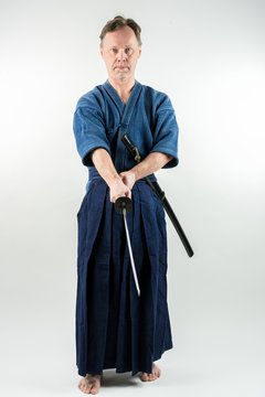 Adult caucasian male training Iaido holding a Japanese sword with focused look. Studio shot with white background.
