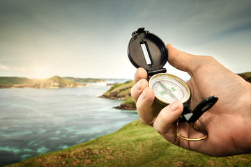 Compass in hand traveler on coastline near ocean on background hills