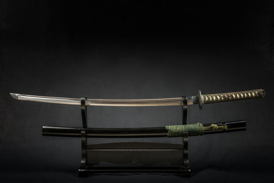Japanese iaido sword in black wooden stand and black background. Still life studio shot with center light. 