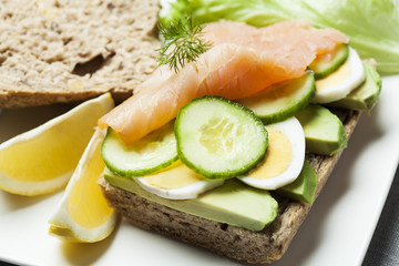 Rye bread sandwich with avocado, eggs, cucumber and smoked salmon