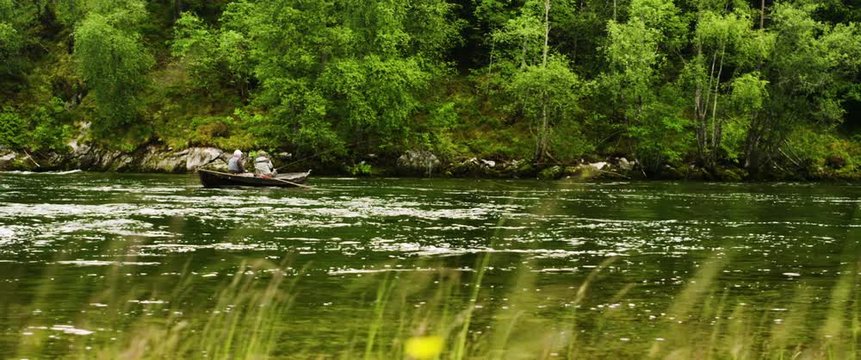 Lockdown shot of senior men rowing boat while fishing on flowing Nordic river
