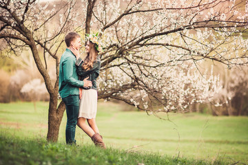 Young couple in love having a date under pink cherry blossom trees in sunset time. Love and tenderness in spring season