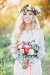 Beautiful blond bride with a wedding bouquet in rays of the sun. Summer wedding.