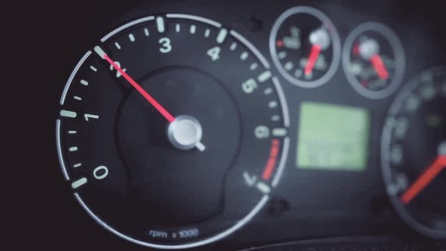 Color close up footage of a car's tachometer revving.