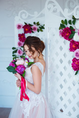 Classical beauty. Beautiful young woman with stylish brunette hair and elegant dress resting in luxury white classic room interior with folding screen and flowers. Spring portrait of elegant bride.