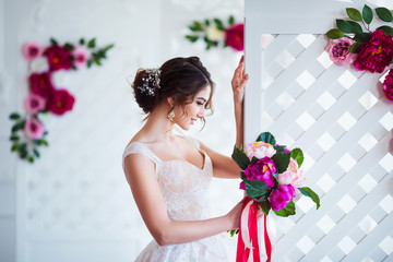 Classical beauty. Beautiful young woman with stylish brunette hair and elegant dress resting in luxury white classic room interior with folding screen and flowers. Spring portrait of elegant bride.