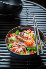 Enjoy your seafood noodle in dark bowl with chopsticks
