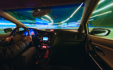 hands on the wheel a car moves at fast speed at the night. Blured road with lights with car on high speed