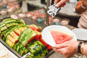 An elderly woman puts a plate of slices of ripe watermelon