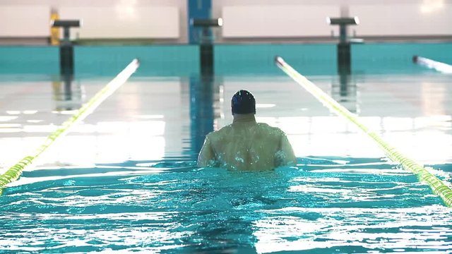 Male swimmer swims in pool HD video. Breaststroke training: comes up and dives. Professional athlete on water lane.
