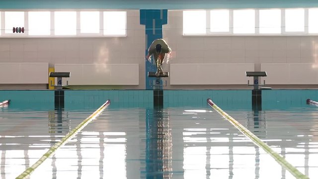 Male swimmer jumps off starting block and start swims in pool HD slow-motion video. Professional athlete training: dive and splashes water surface