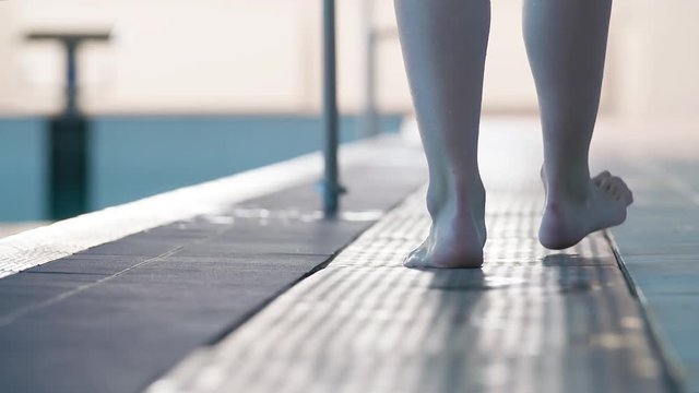 Female swimmer barefoot leg foots walking on swimming pool rubber flooring HD slow-motion video. Back view of ankle and foot steps of athlete