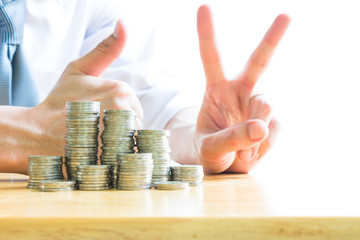 Stack of coins on wooden table over blurred businessman with thumb up background, business and finance concept