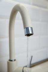 Beige faucet in the kitchen on a background of white tiles 