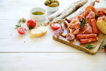 Antipasto with traditional Spanish meat snacks on wooden board and white wooden background