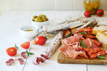 Antipasto with traditional Spanish meat snacks on wooden board and white wooden background