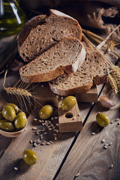 Fresh multigrain crusty bread, green olives and wheat ears on a