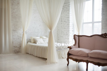 Bedroom in soft light colors. Big comfortable elegant double bed in white brick loft interior with...