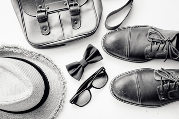 Men's accessories outfits with leather shoes, bag, hat, sunglasses, and bow tie, top view, flat lay on wooden board background, black and white