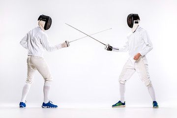 The two men wearing fencing suit practicing with sword against gray