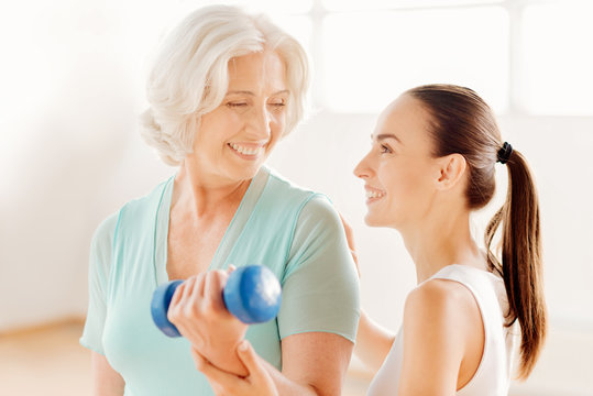 Nice fitness coach helping the elderly woman