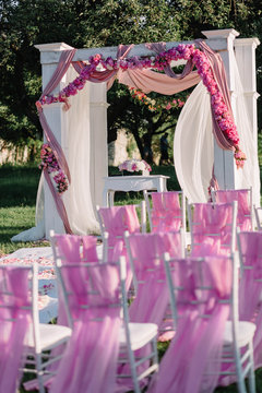 arch for the wedding ceremony and pink chairs standing outdoors