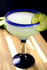 Margarita with lime slice in a blue rimmed glass on a wood surface
