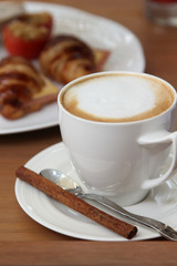 Hot cappuccino coffee in white cup with cinnamon stick.